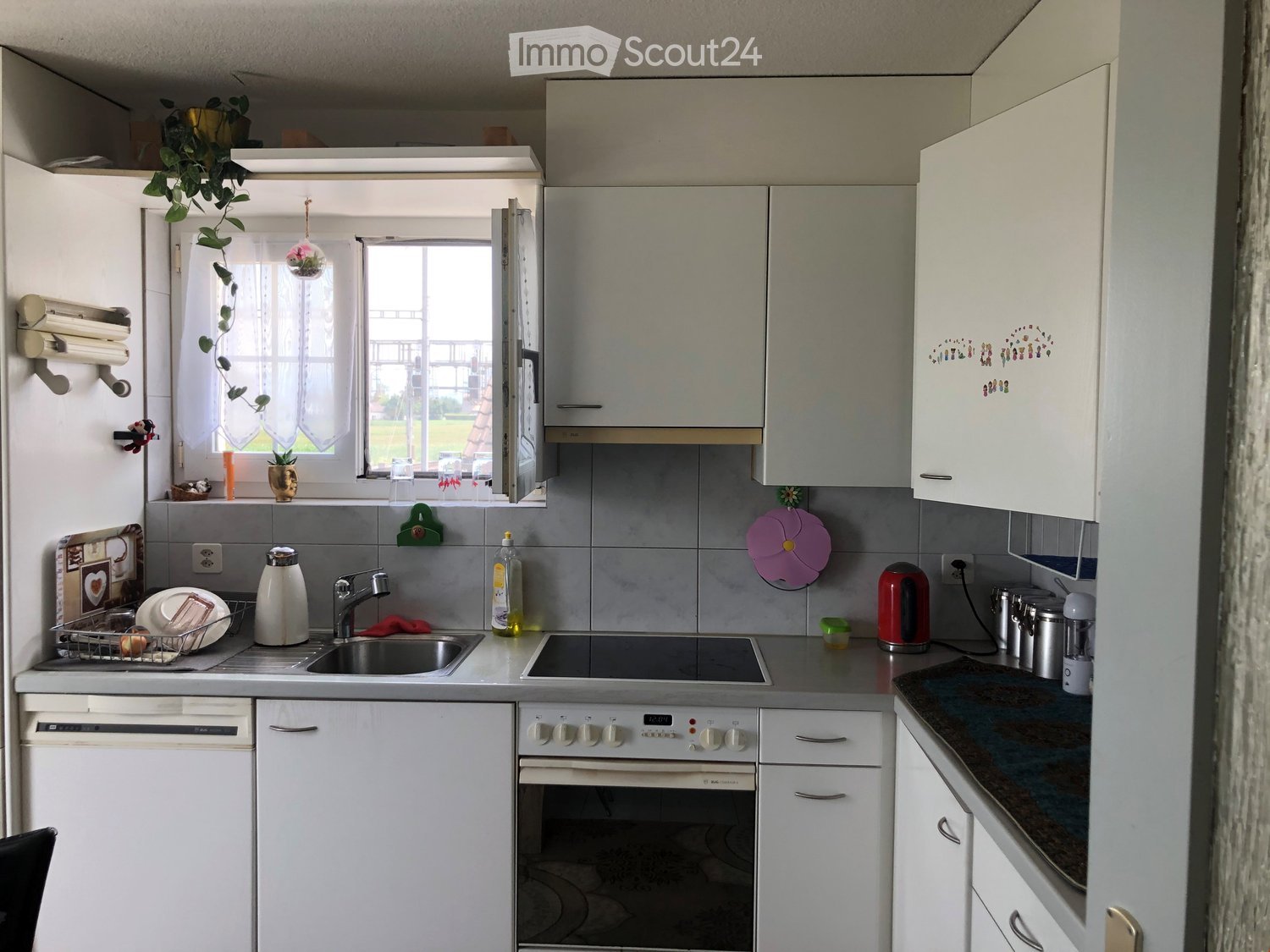 Modern kitchen with white cabinets, stainless steel appliances, and a window with a view of the outdoors. The counter features a sink, electric kettle, and various small appliances.