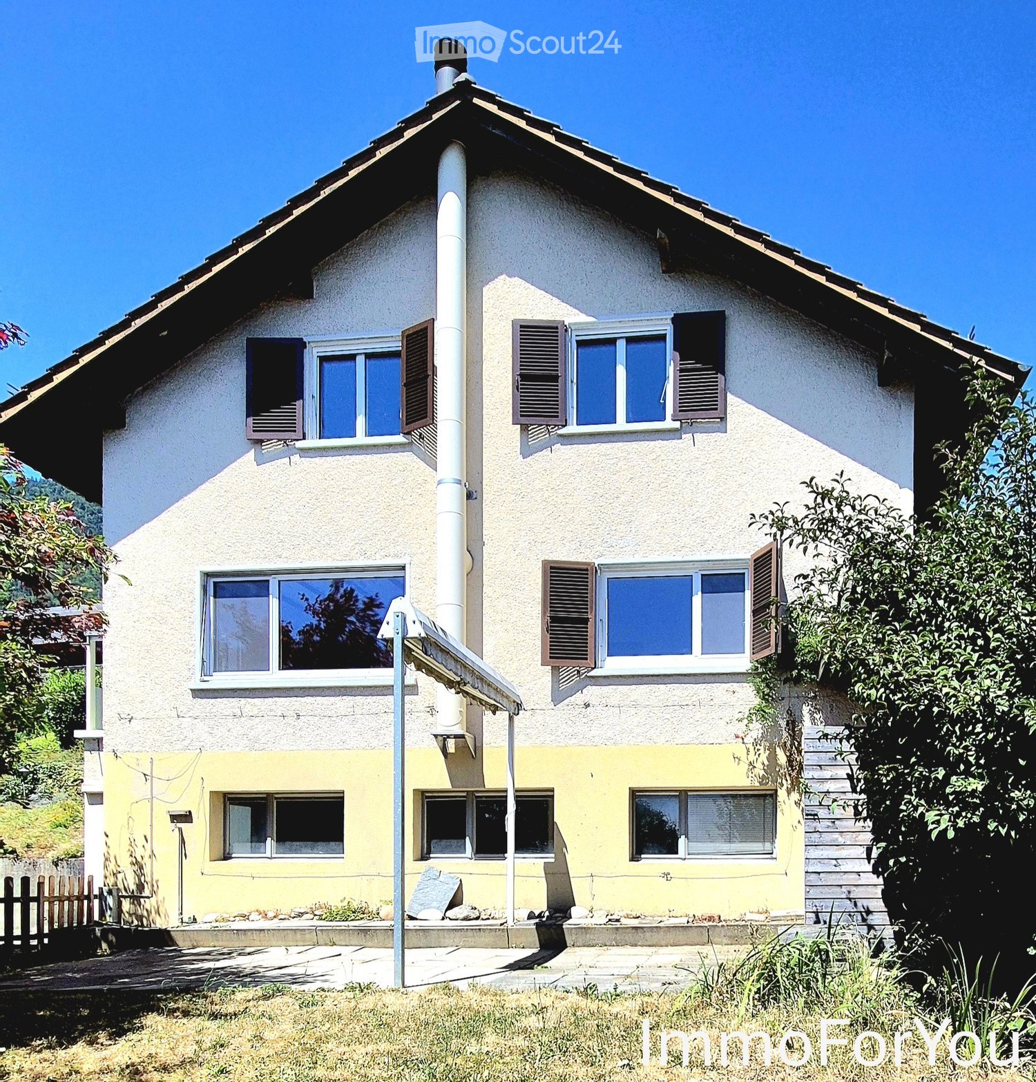 Two-story house with white and yellow exterior, multiple windows with shutters, and a small garden area.