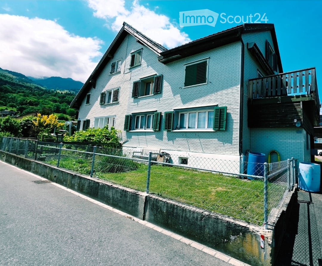 Two-story white brick house with green shutters, balcony, and scenic mountain view.