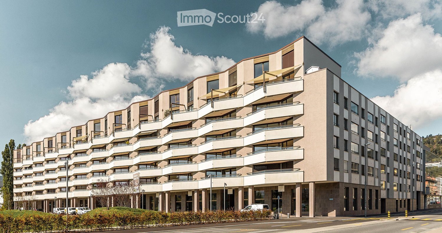 Modern multi-story residential building with balconies and large windows, featuring a contemporary design with beige and grey tones.