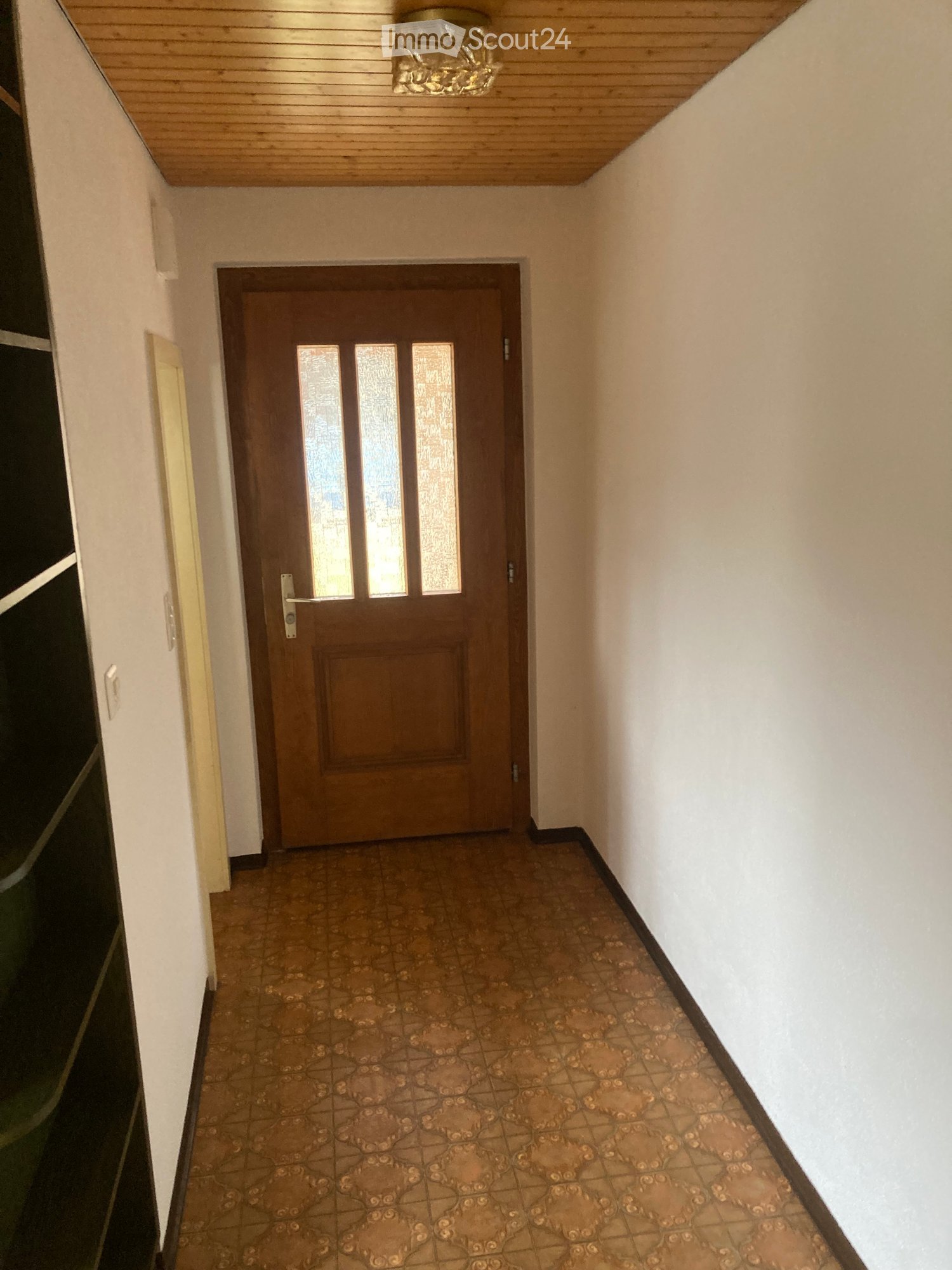 Hallway with a wooden door, tiled floor, and light fixture on the ceiling.