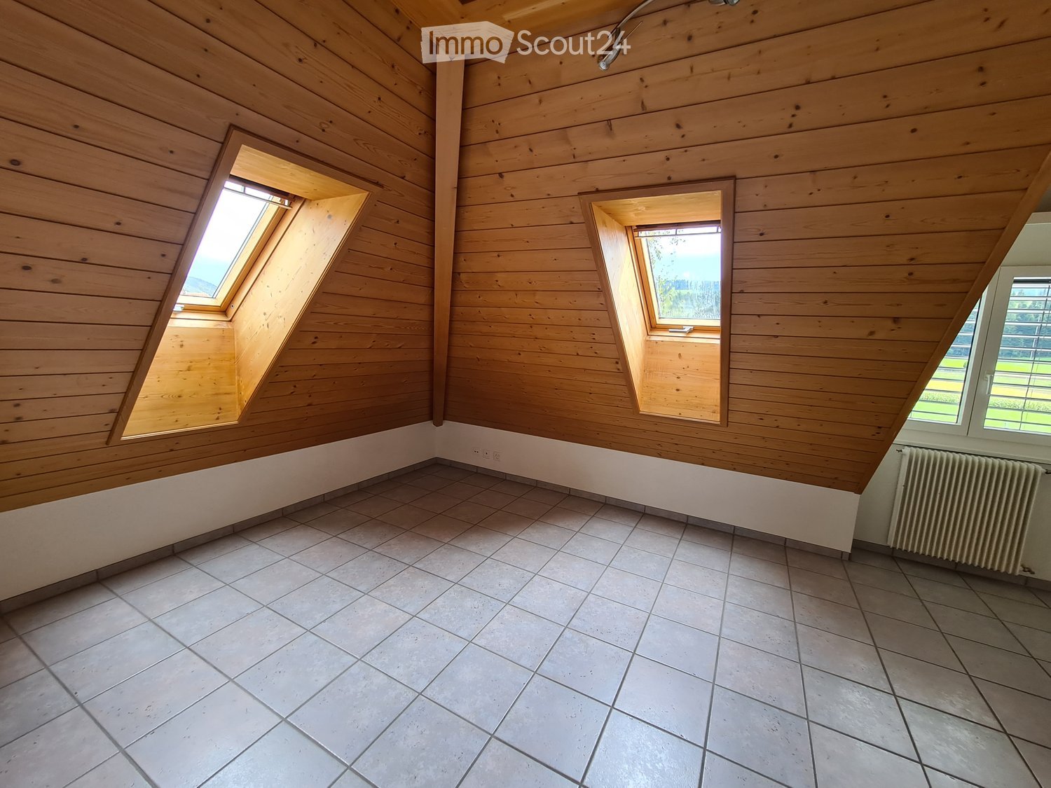 Empty attic room with wooden walls, slanted wooden ceiling, tiled floor, and multiple windows including skylights.