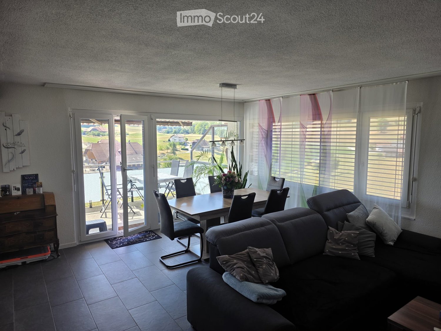 Living and dining area with a grey sectional sofa, dining table with chairs, sideboard, and a view of the outdoor patio.