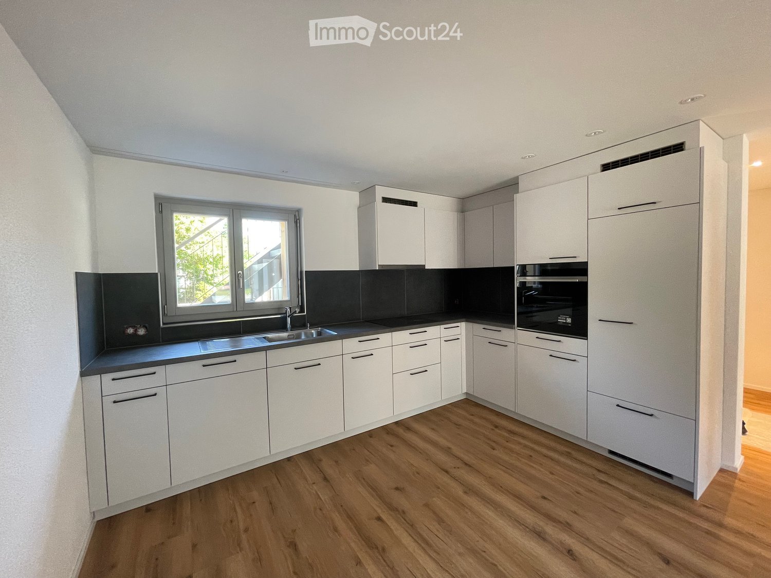 Modern kitchen with white cabinets, wooden flooring, and a black countertop. Features a sink, faucet, and built-in oven.