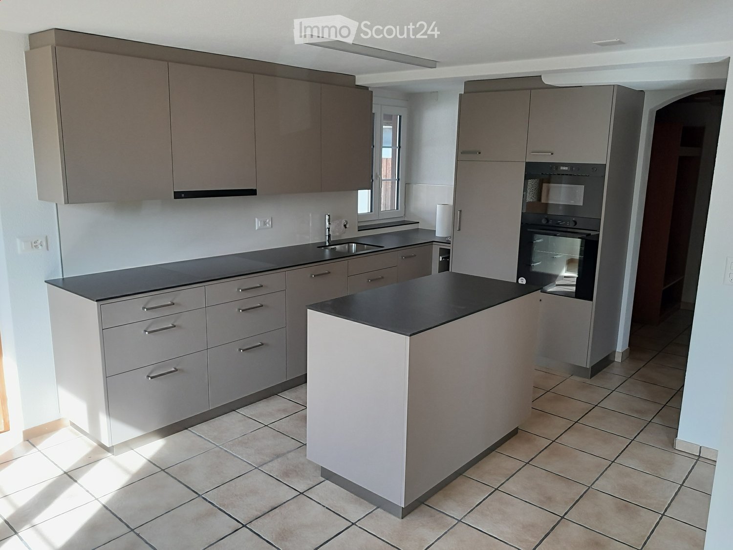 Modern kitchen with grey cabinets, black countertops, and a central island. Features include a sink, oven, and ample storage space.