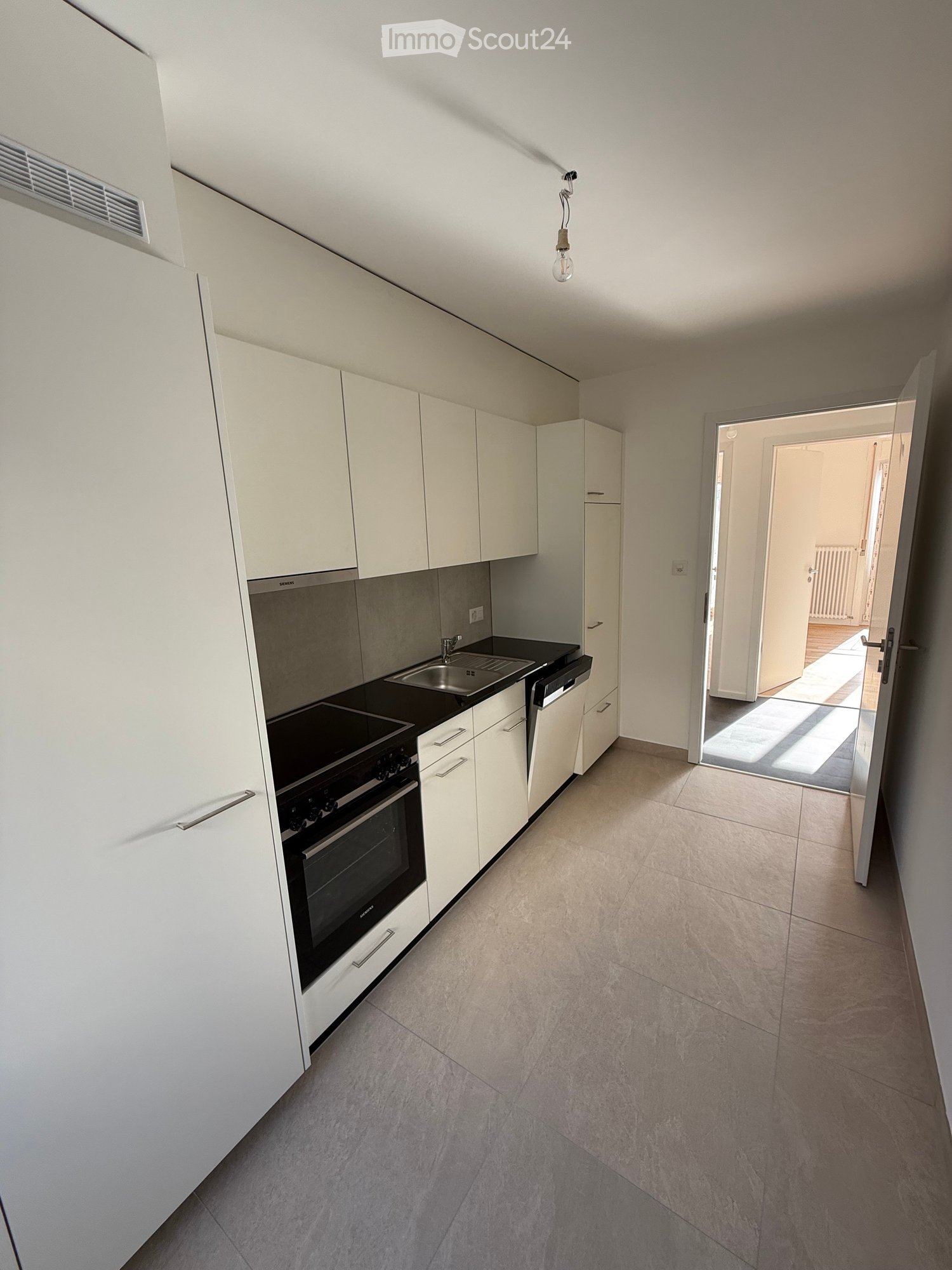 Modern kitchen with white cabinets, black countertop, built-in oven, sink, and dishwasher. Open doorway leads to another room.