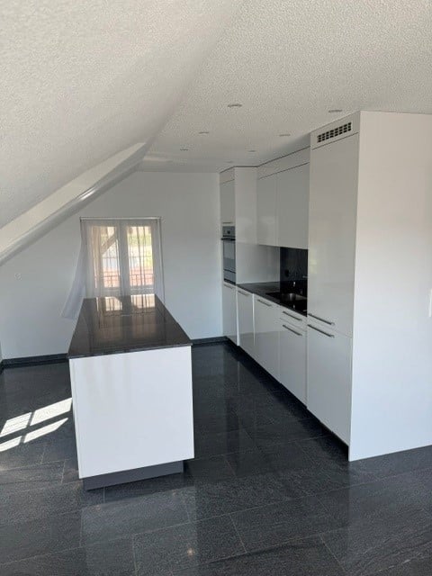 Modern kitchen with white cabinets, black countertops, and a central island. Features include an oven, sink, and ample storage space.