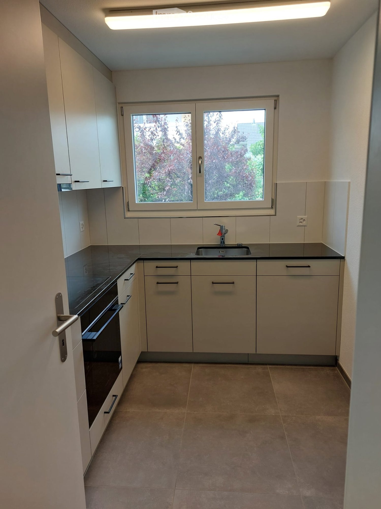Empty kitchen with white cabinets, black countertops, a sink, and a window overlooking greenery.