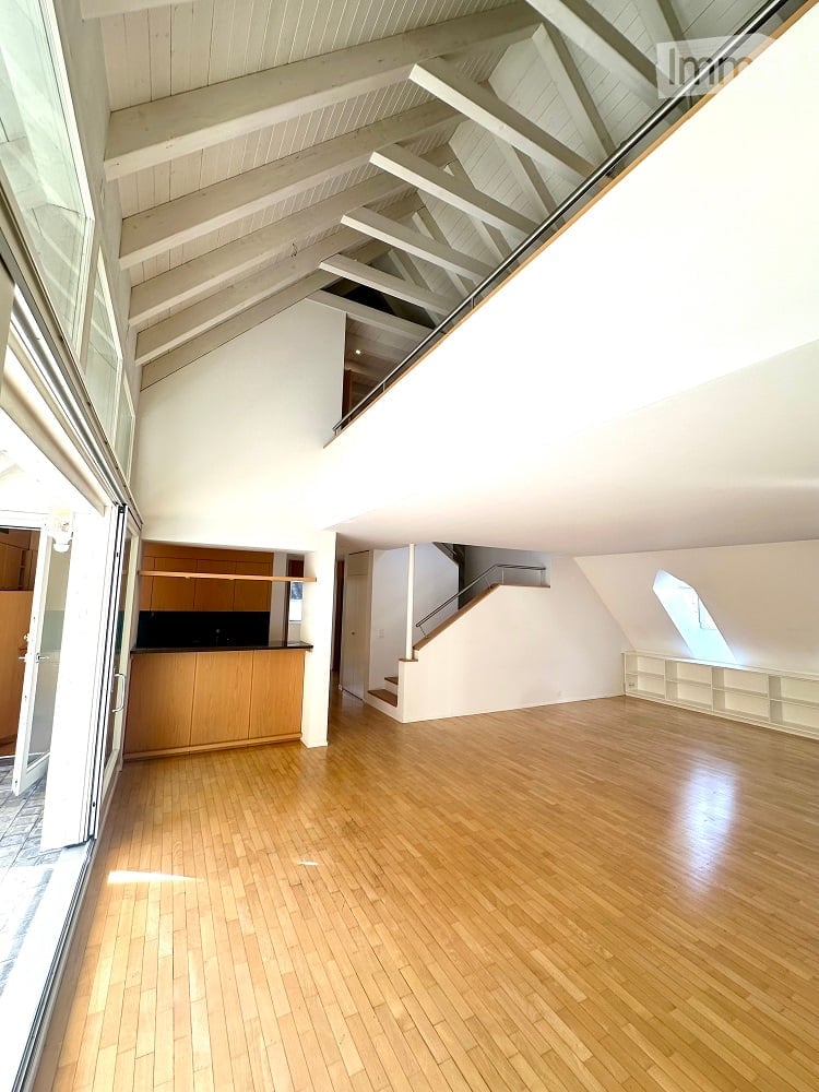 Large open living area, wooden floor, white walls, white ceiling, balcony, kitchen, wooden cabinets, stairs