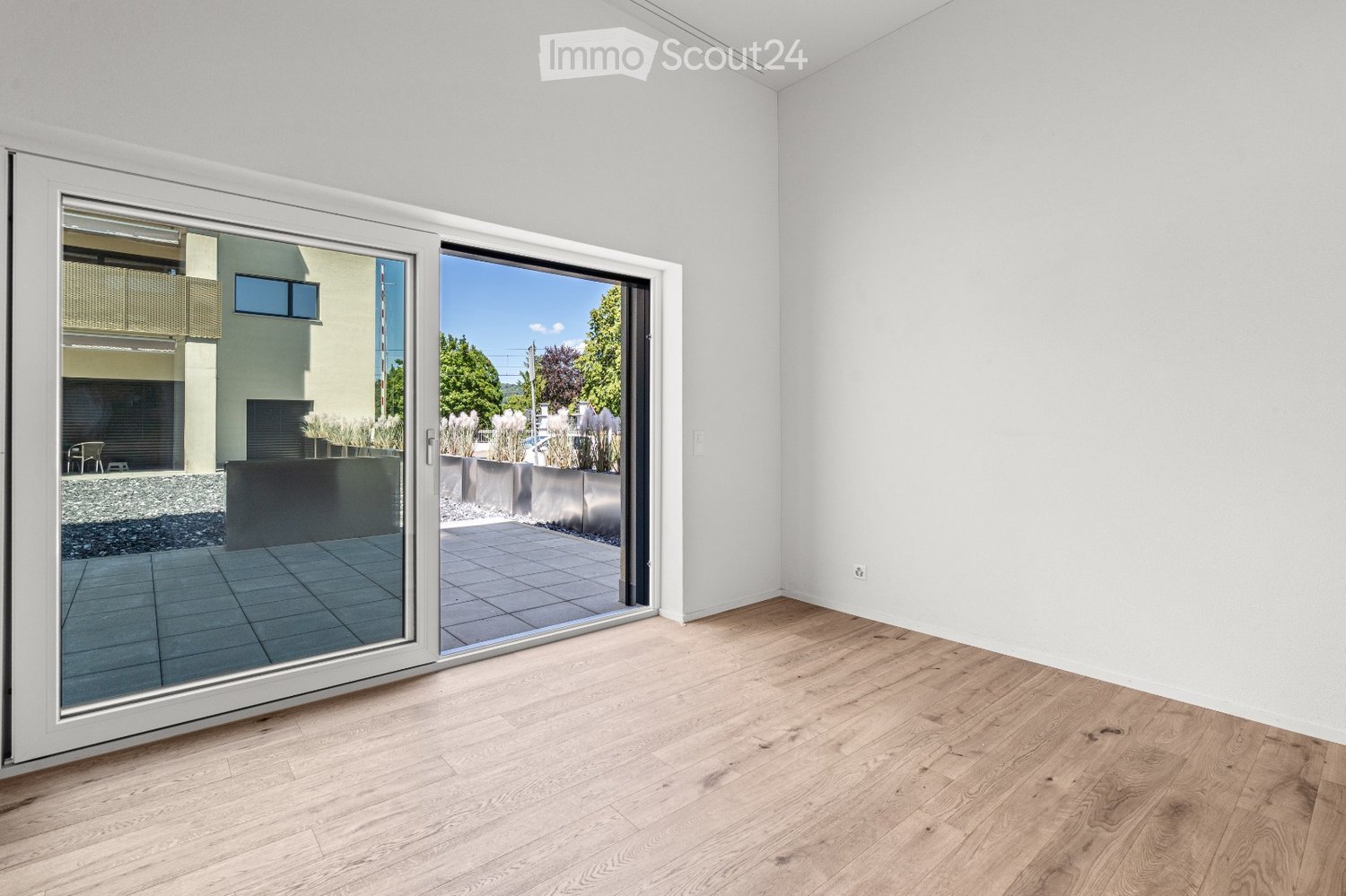 Empty room with light wooden flooring and large sliding glass doors leading to a tiled outdoor area.