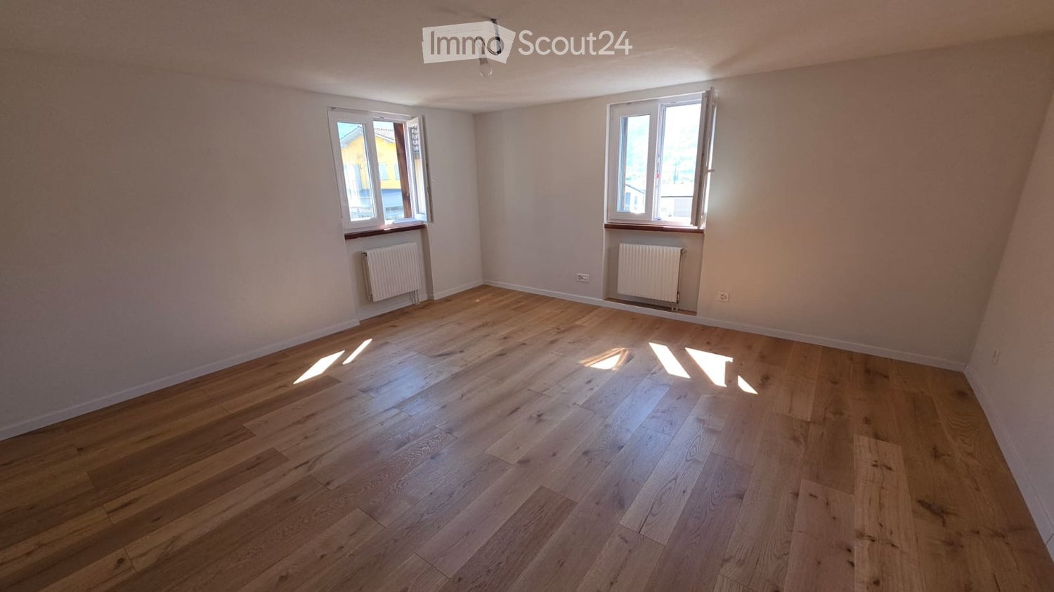 Empty room with wooden flooring, white walls, two windows, and radiators under each window.