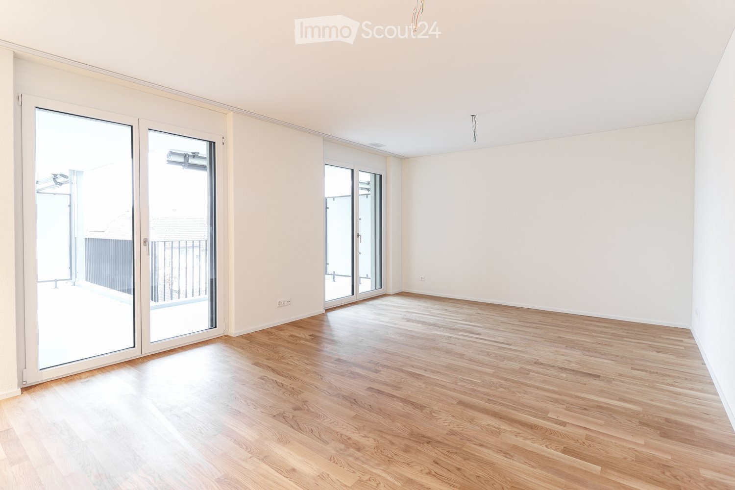Empty room with light wooden flooring, white walls, and large glass sliding doors leading to a balcony.