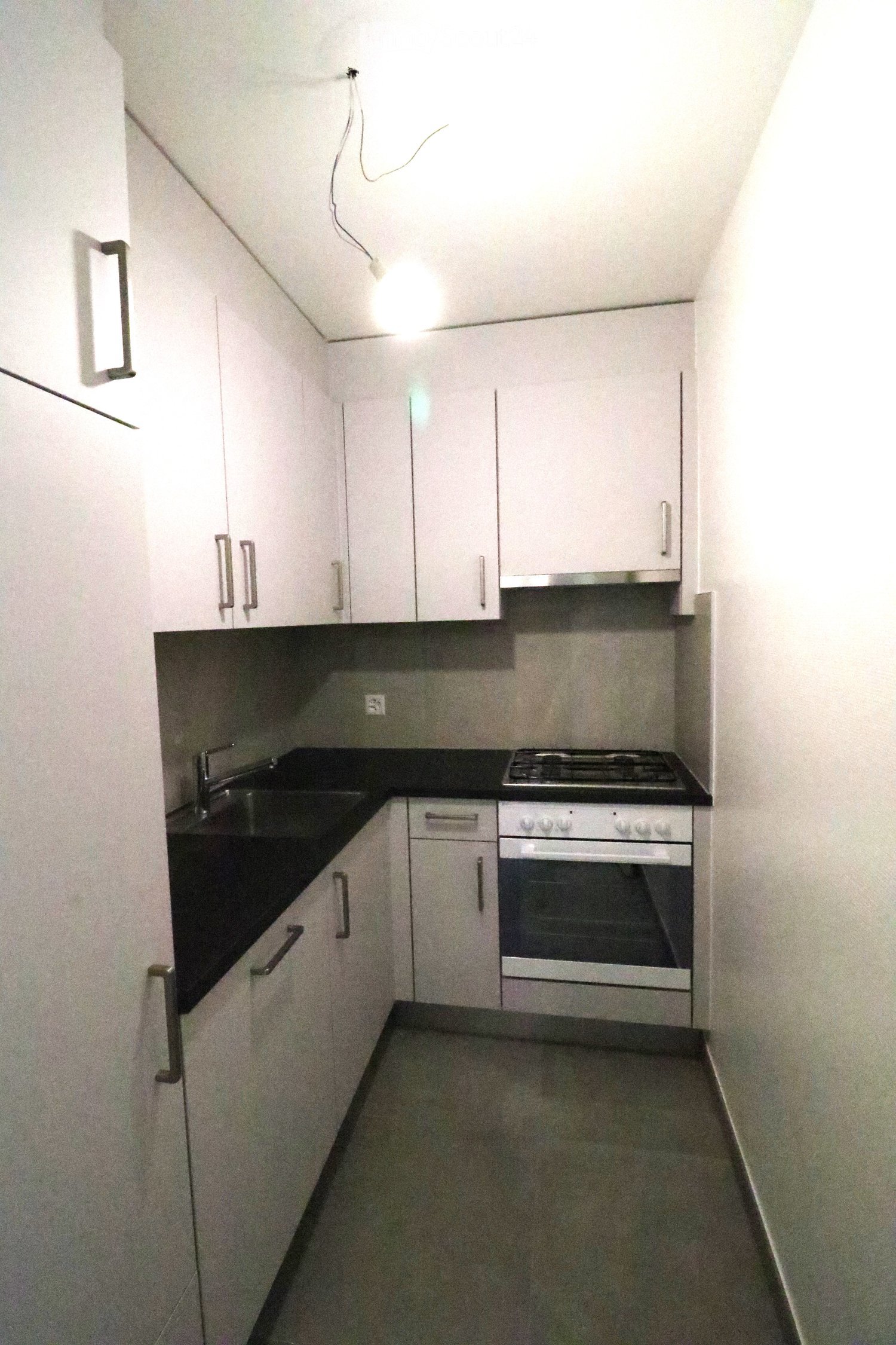Modern kitchen with white cabinets, black countertops, and stainless steel appliances including a sink, stove, and oven.