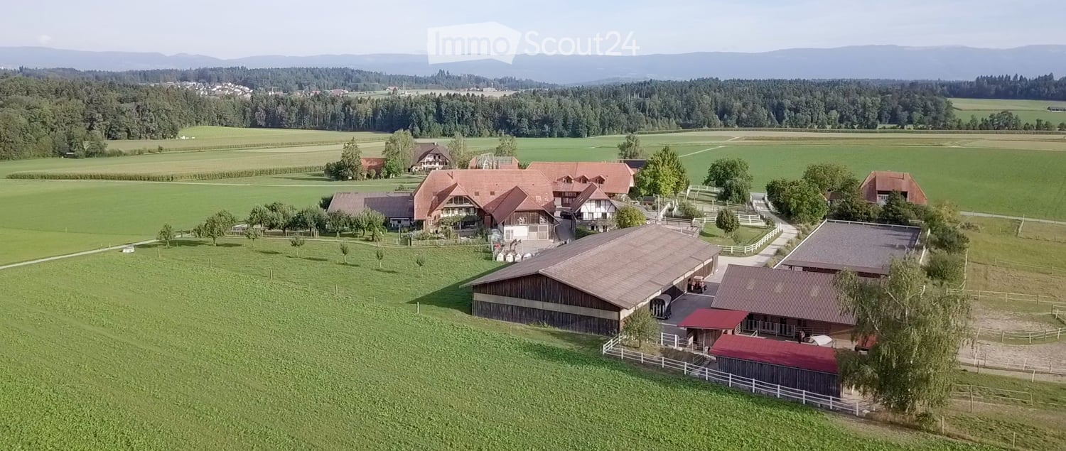 Aerial view of a large rural estate with multiple buildings, including a main house, barns, and outbuildings, surrounded by green fields and trees.