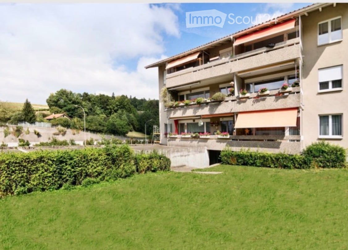 Multi-story apartment building with balconies, greenery, and a well-maintained lawn in front.