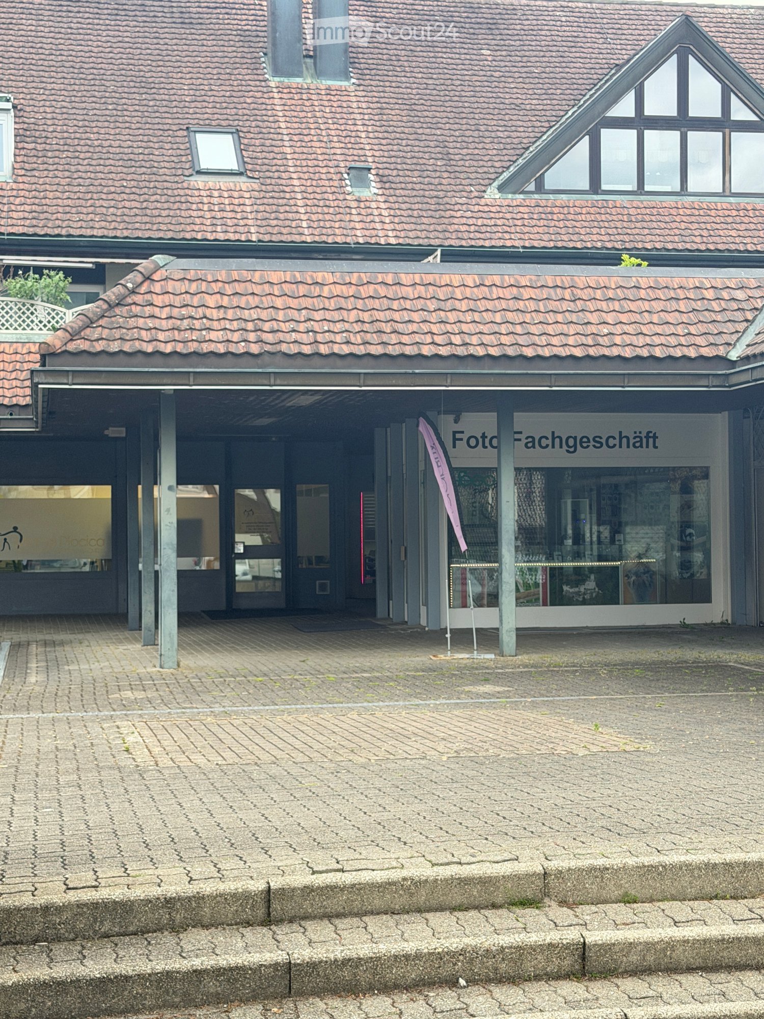 Two-story building with a tiled roof, a covered entrance area, and signage reading "Foto Fachgeschäft" (photo shop).