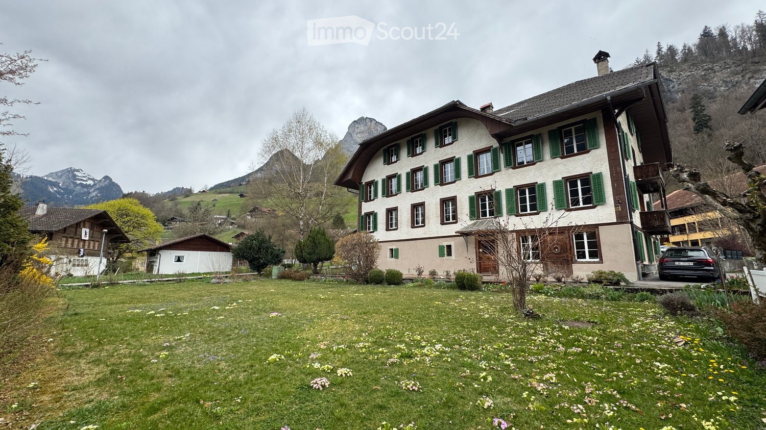 3 story building, green shutters, white walls, garden, mountains in the background