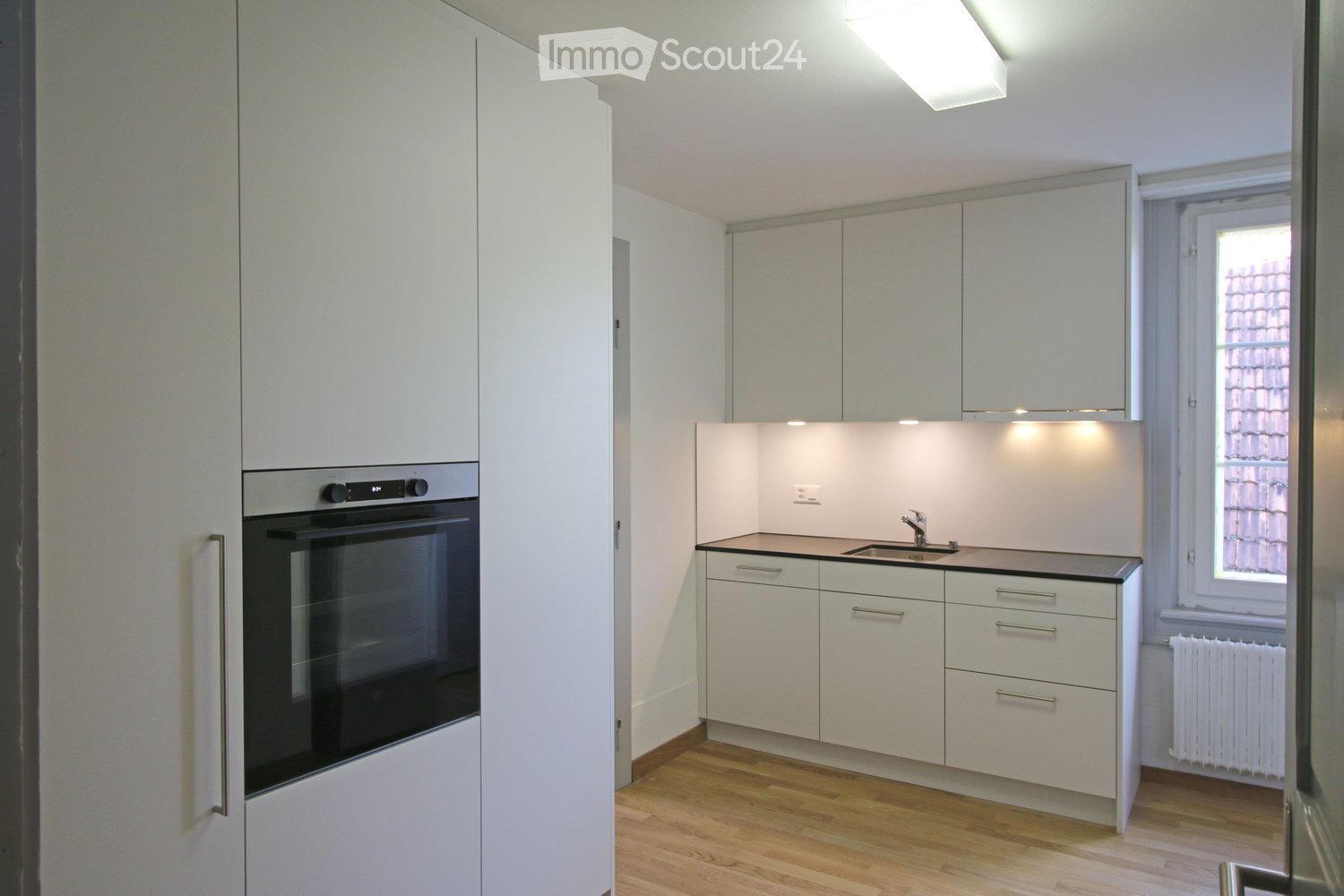 Modern kitchen with white cabinets, a built-in oven, a sink with a faucet, and a radiator under the window.