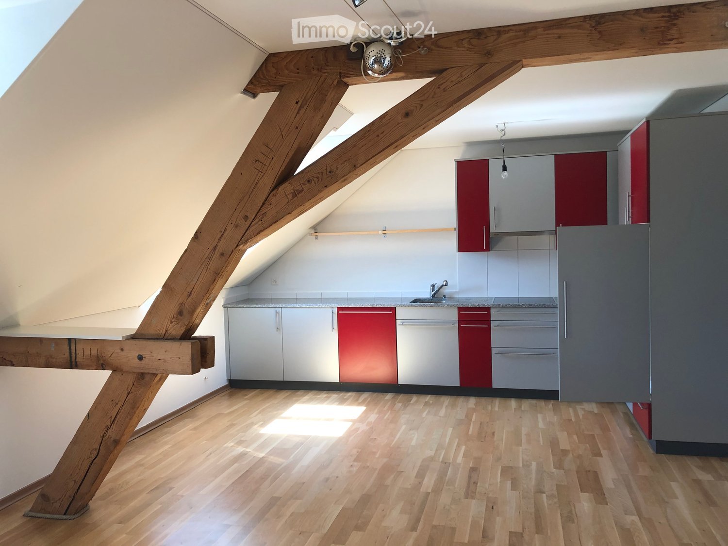 Modern kitchen with wooden beams, light wooden flooring, and red and grey cabinets.