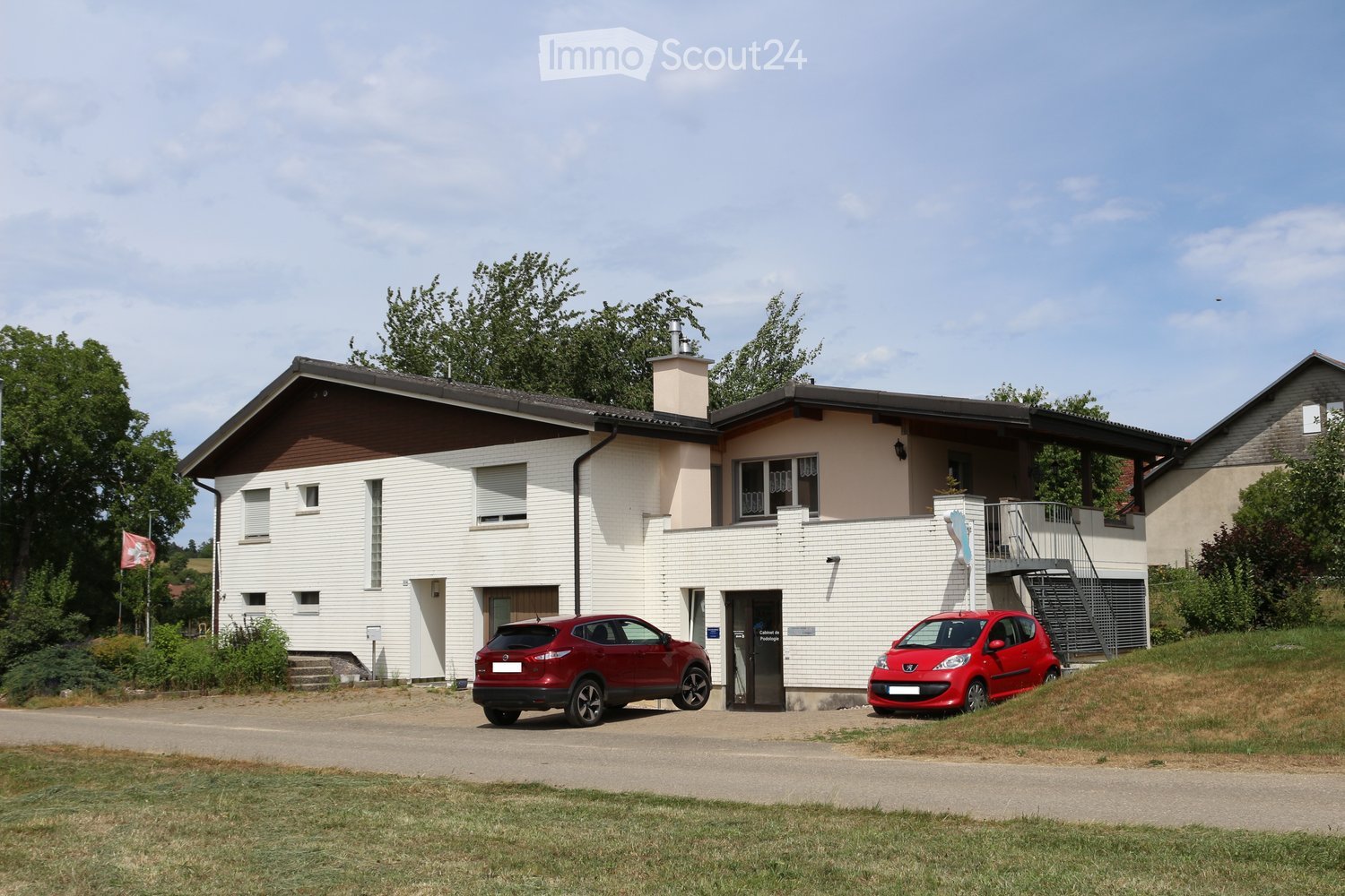 Two-story house with white siding, brown roof, garage, and two parked cars.