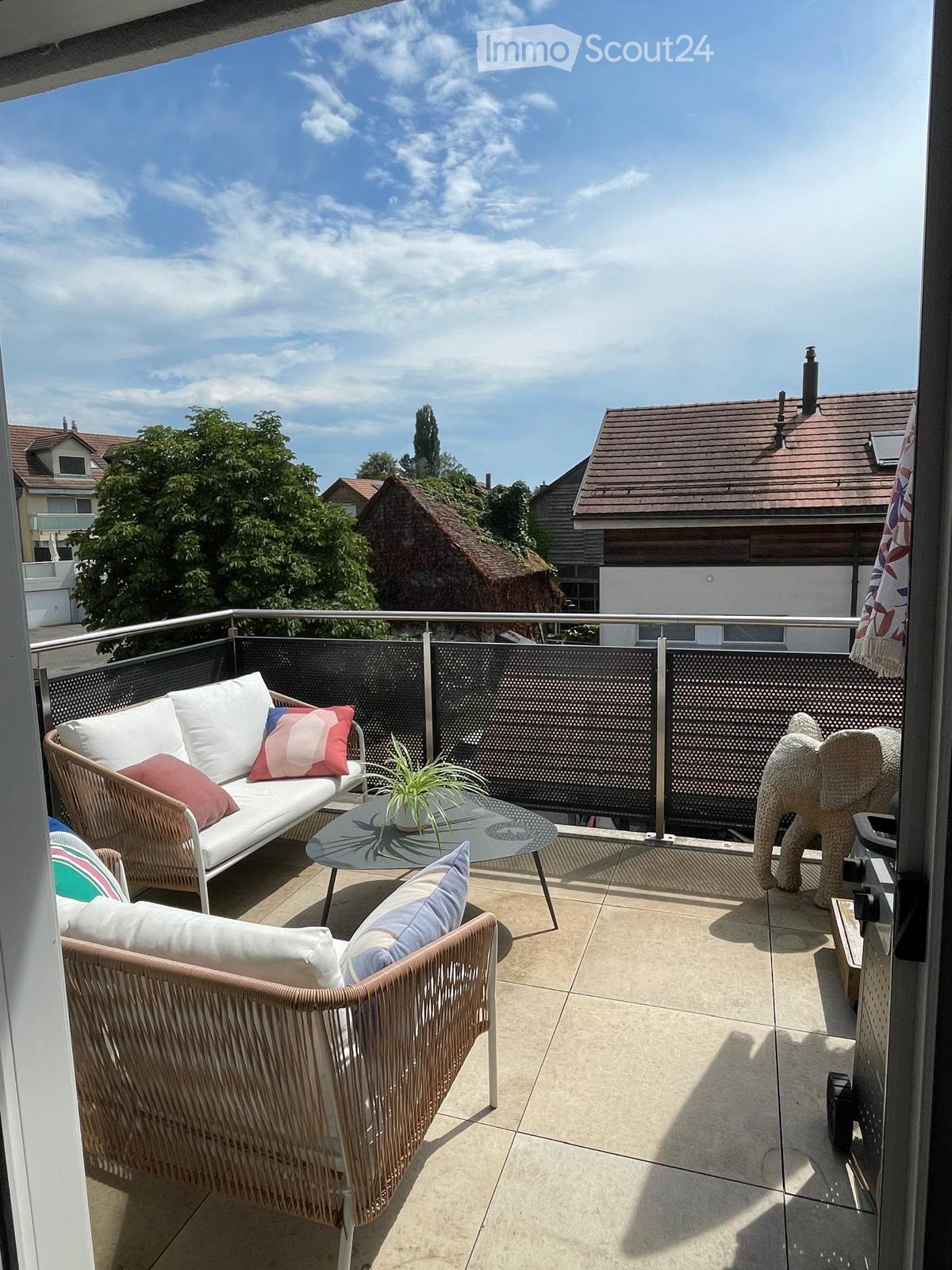 Balcony with a white sofa, two wicker chairs, a glass coffee table with a small plant, and a decorative elephant-shaped stool.