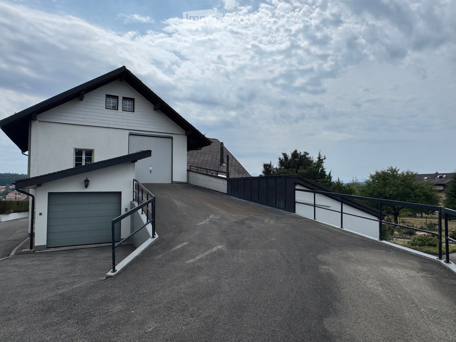 Two-story house with white siding, grey garage doors, and a raised driveway leading to the entrance.
