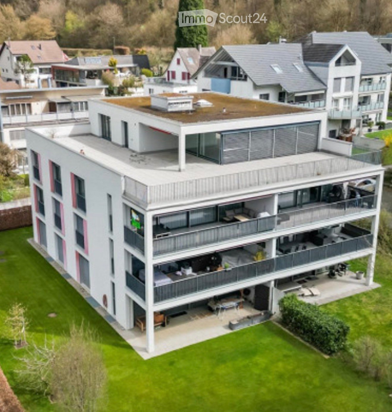 Modern multi-story house with white exterior, grey roof, multiple balconies, and a green lawn in front.