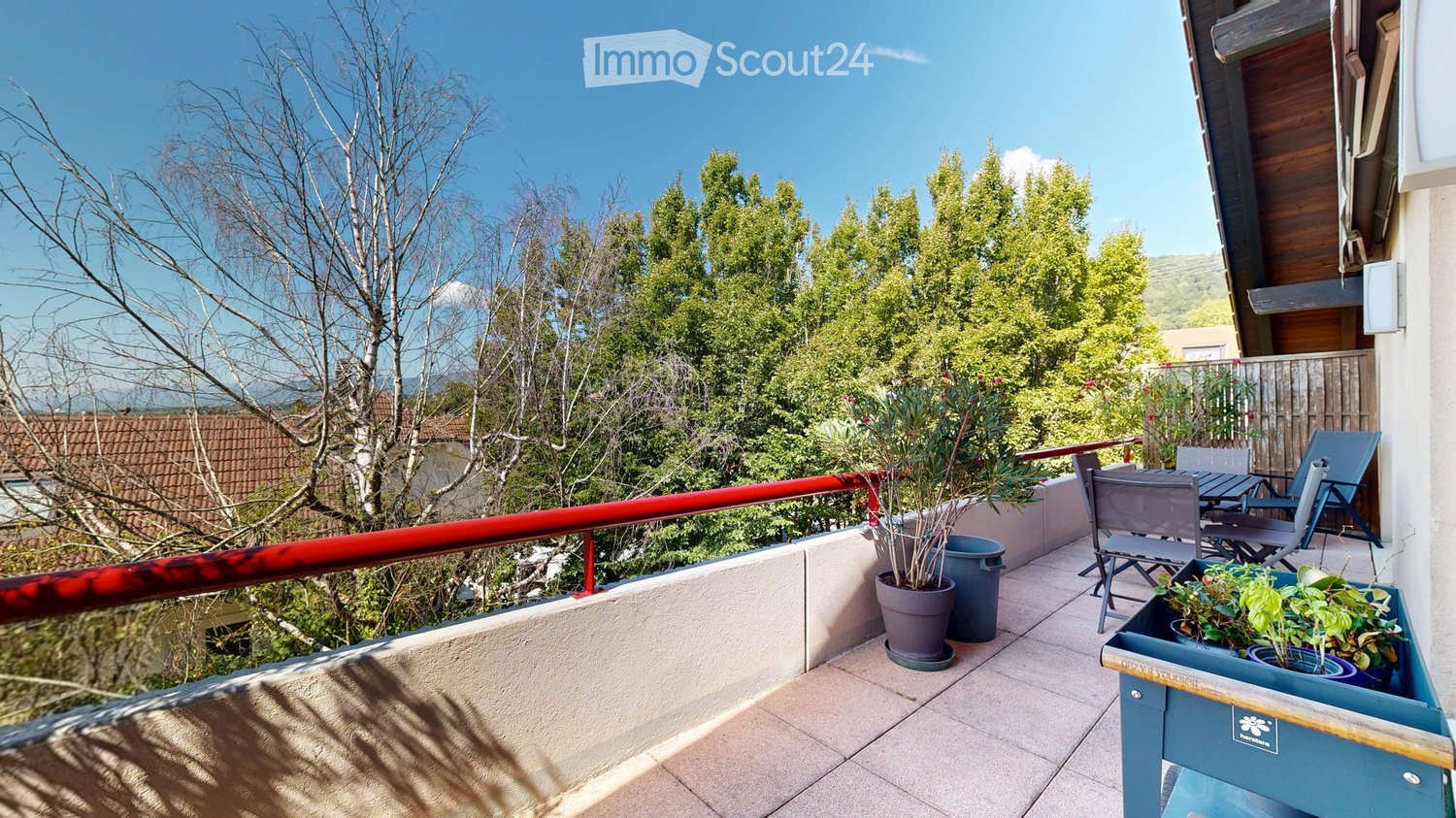 Red railing, white floor, potted plants, outdoor table and chairs, green trees, sunny weather