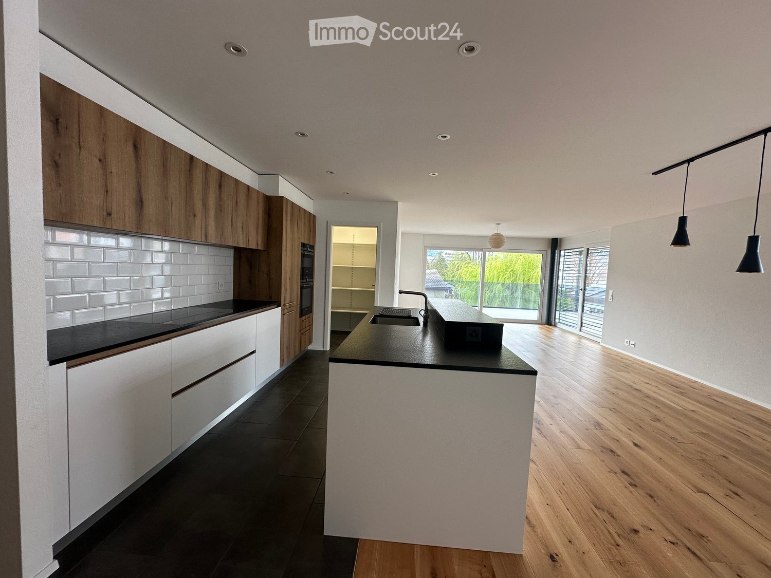 Modern kitchen with wooden and white cabinets, black countertops, and a central island. Features include a sink, faucet, and built-in oven.