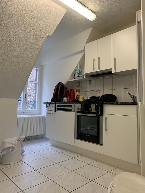 Modern kitchen with white cabinets, tiled floor, and an oven. A backpack and some items are placed on the counter.
