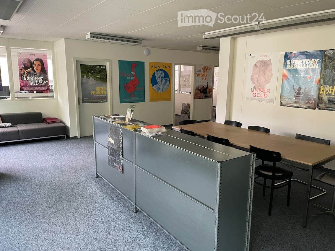 Office space with a reception desk, sofa, table with chairs, and several posters on the walls.