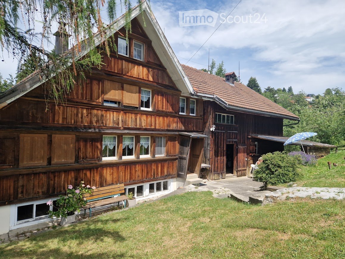 Traditional wooden house with a red-tiled roof, multiple windows, and a small garden area with a bench and potted plants.