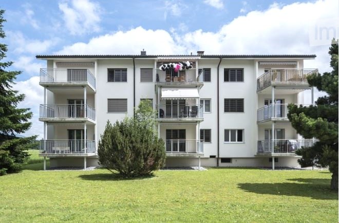 Multi-story residential building with multiple balconies and a well-maintained lawn in front.