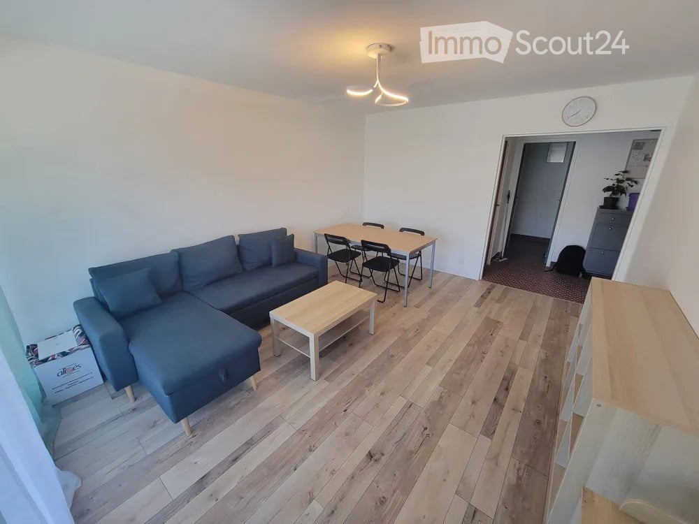 Modern living room with light wooden flooring, a blue sectional sofa, a white coffee table, and a small dining area with a table and chairs.
