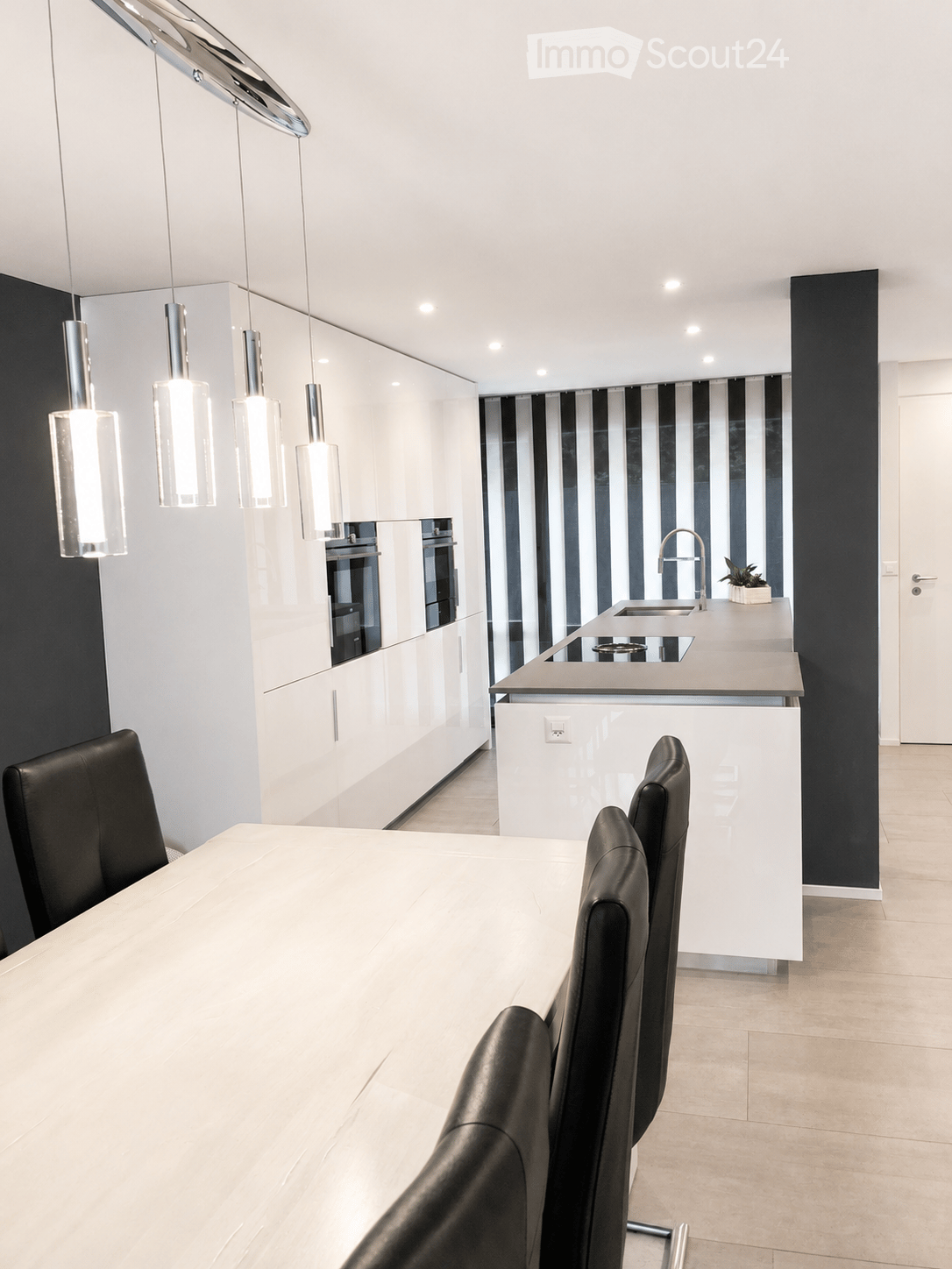 Modern kitchen and dining area with white cabinets, a central island, pendant lights, and a dining table with black chairs.