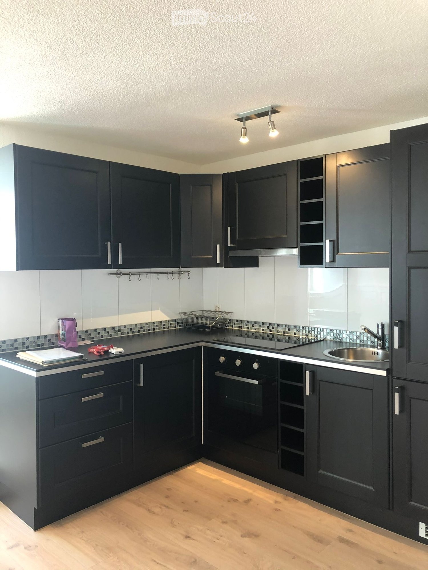 Modern kitchen with dark cabinets, stainless steel sink, oven, and countertop items including a purple bag and papers.