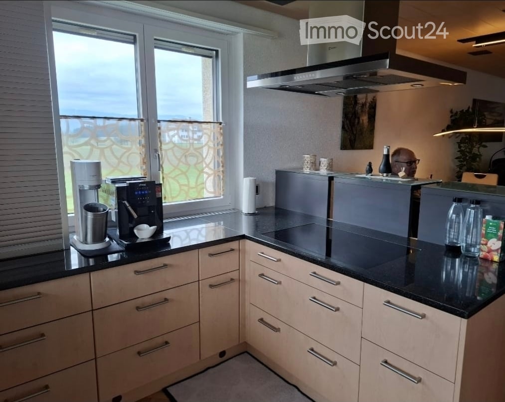 Modern kitchen with light wood cabinets, black countertops, stainless steel appliances, and a large window offering a scenic view.