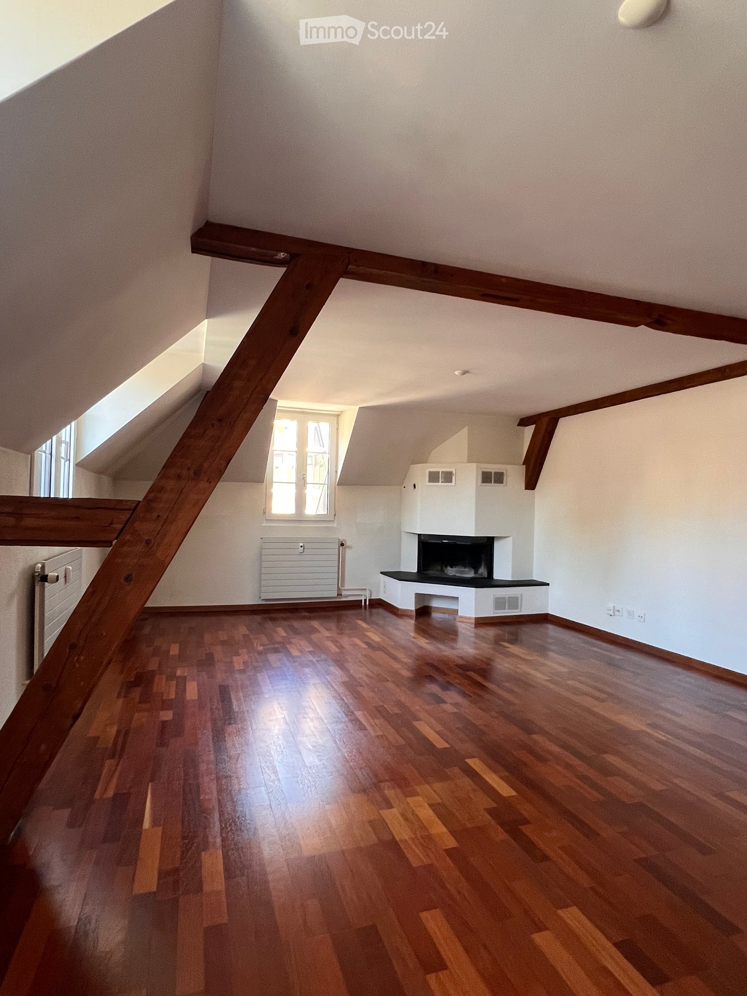 Empty room with wooden flooring, white walls, and a fireplace. Natural light from skylights and windows.