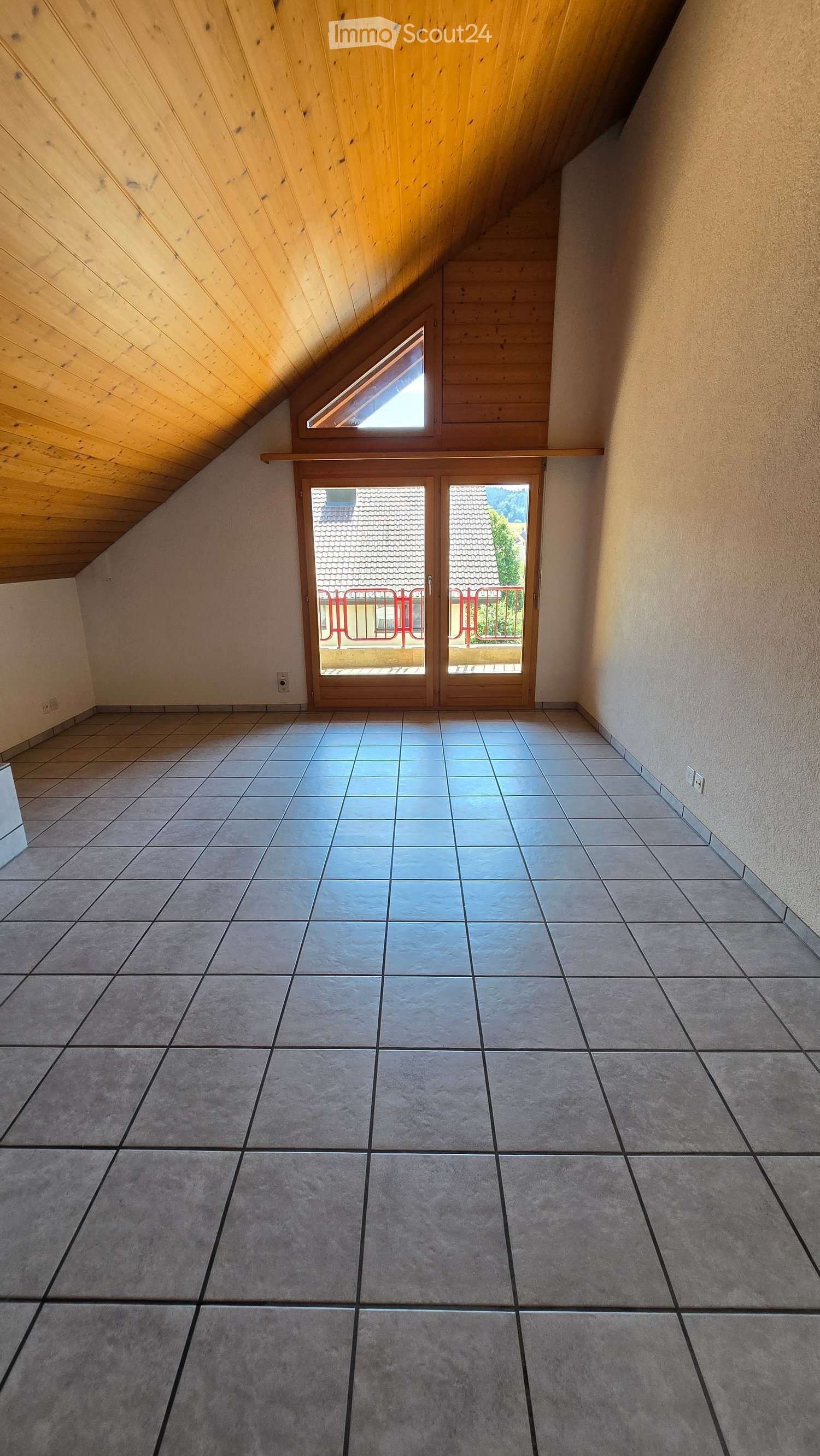 Empty room with tiled floor, wooden ceiling, and sliding glass doors leading to a balcony.