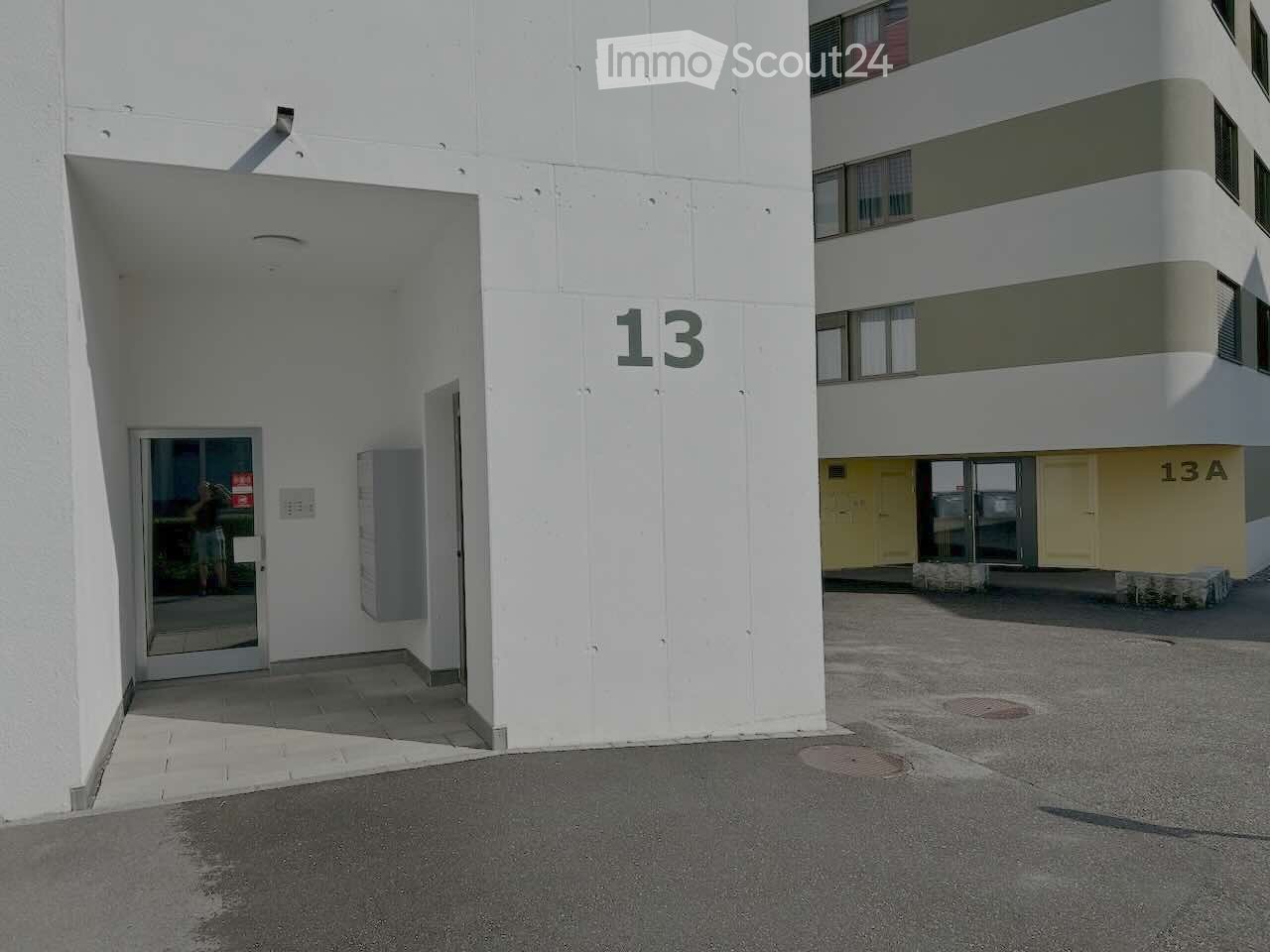 Exterior view of a modern multi-story building with white walls and numbered entrances, including unit13 and 13A.