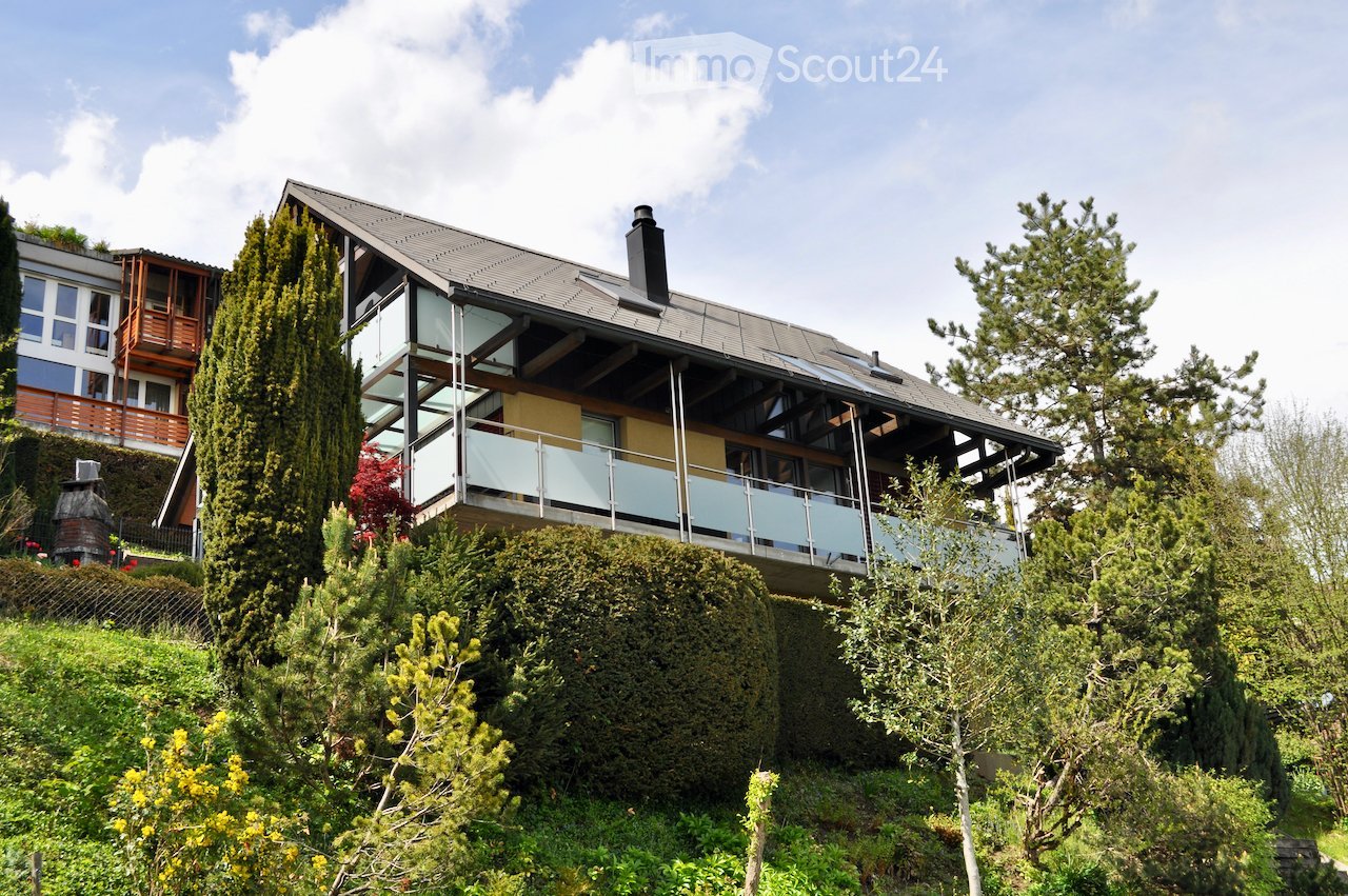 modern house, glass balcony, gray roof, surrounded by trees and bushes