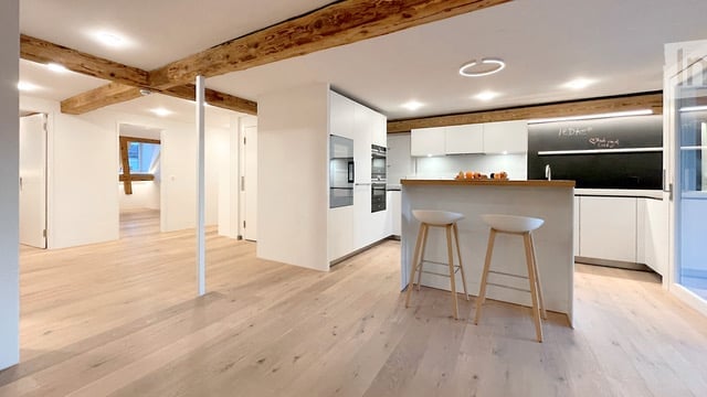Modern kitchen with light wood flooring, white cabinetry, built-in appliances, and a central island with bar stools.