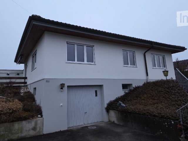 Two-story house with white exterior, grey garage door, multiple windows, and a small garden area.