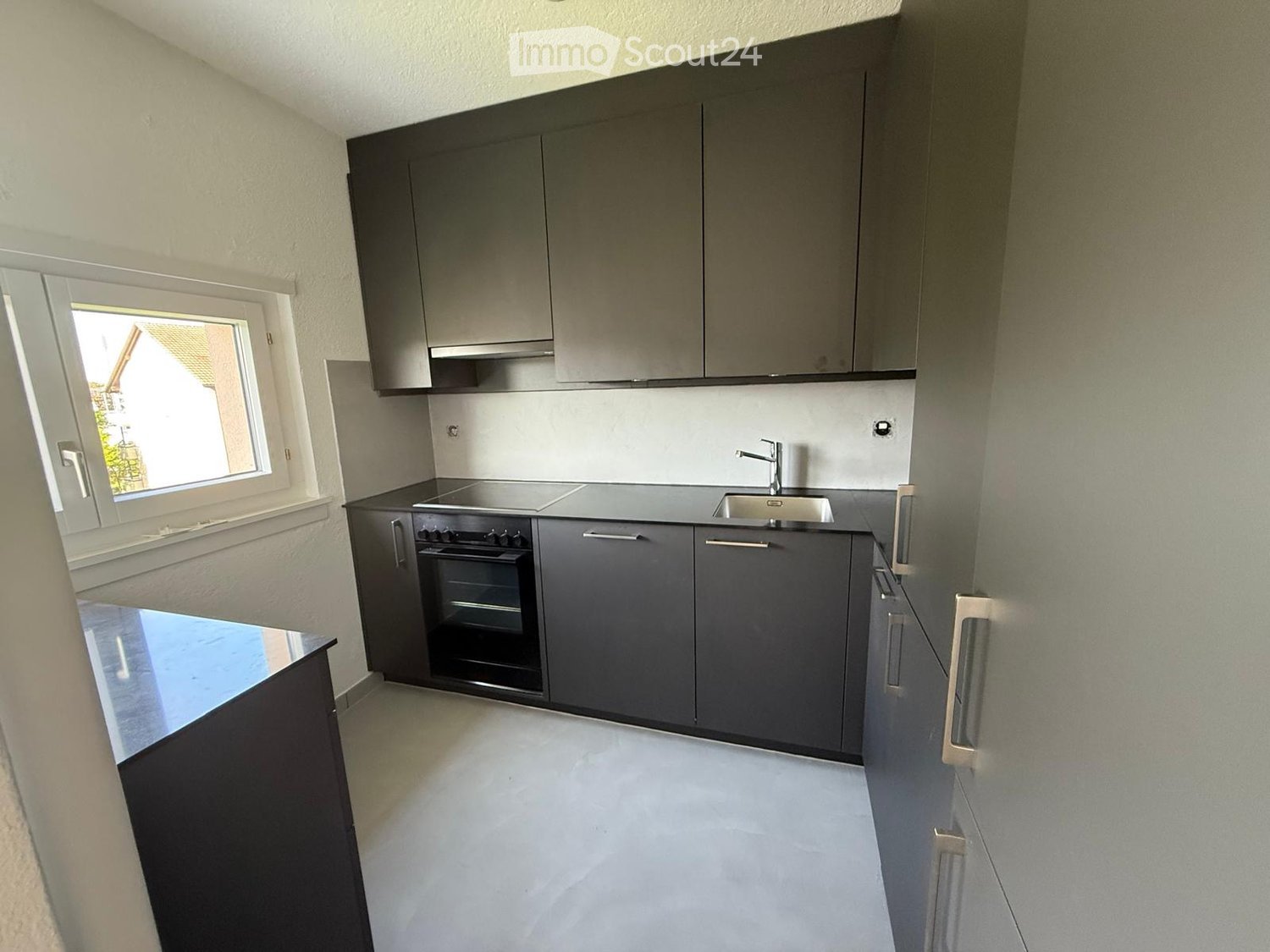 Modern kitchen with grey cabinets, stainless steel sink, and built-in oven. Features a large window with a view of the outside.