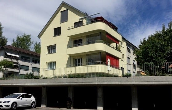 Modern multi-story residential building with balconies, garage, and a parked car in front.