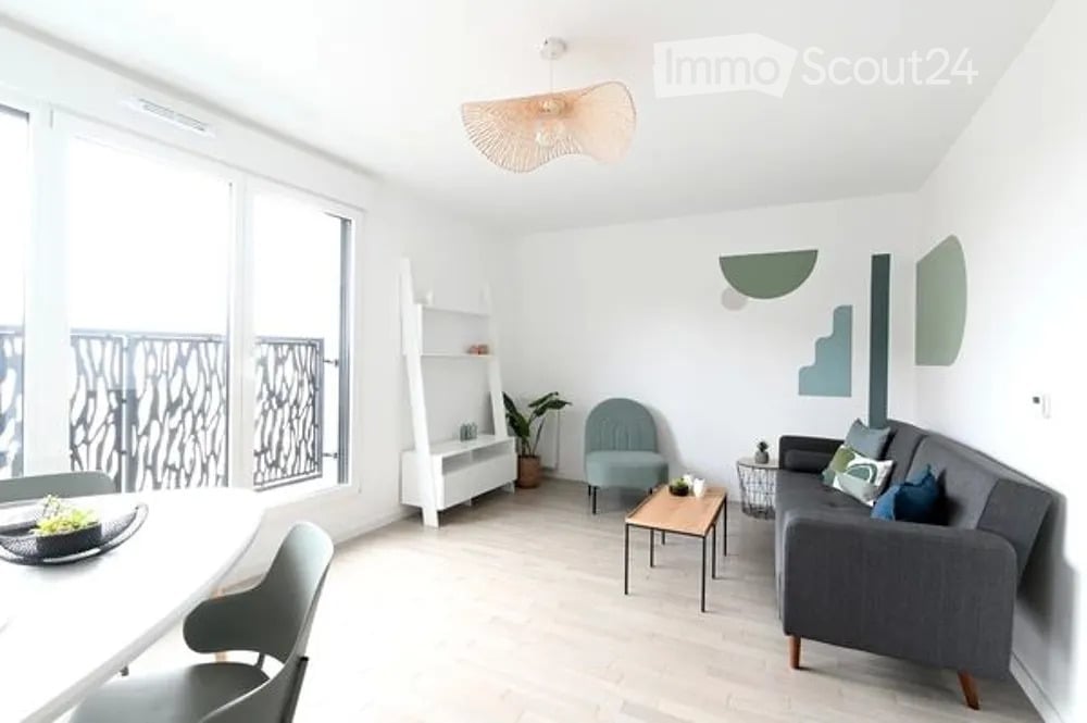 Modern living room with large windows and balcony access, featuring a grey sofa, coffee table, armchair, shelf, and dining area with a table and chairs.