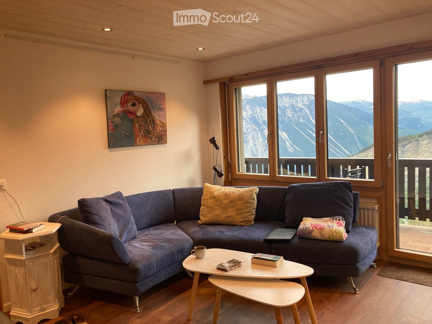 Living room with a blue sectional sofa, coffee table, small stool, and large windows offering a mountain view.