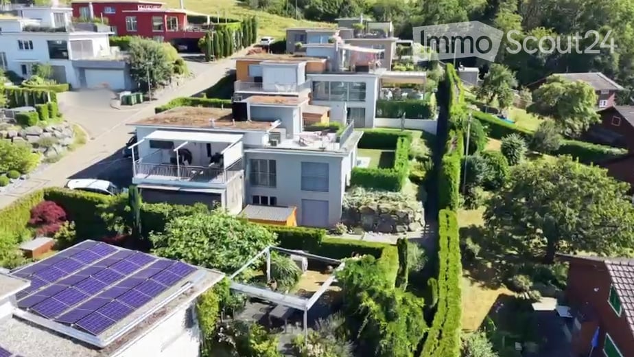 Aerial view of a residential neighborhood with multiple modern houses, well-maintained gardens, and solar panels on one roof.