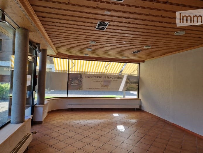 Empty room with tiled floor, wooden ceiling, large windows, and a curved wall. No furniture or equipment present.