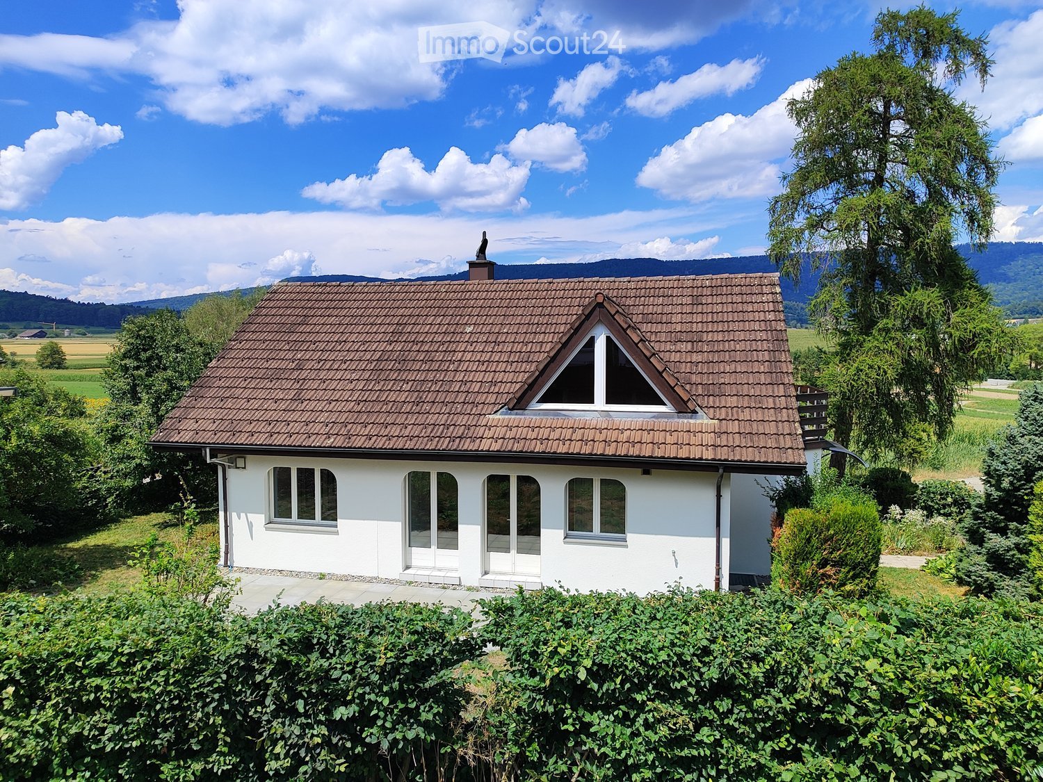 Single-story white house with brown tiled roof, multiple windows, and a small dormer window on the roof.